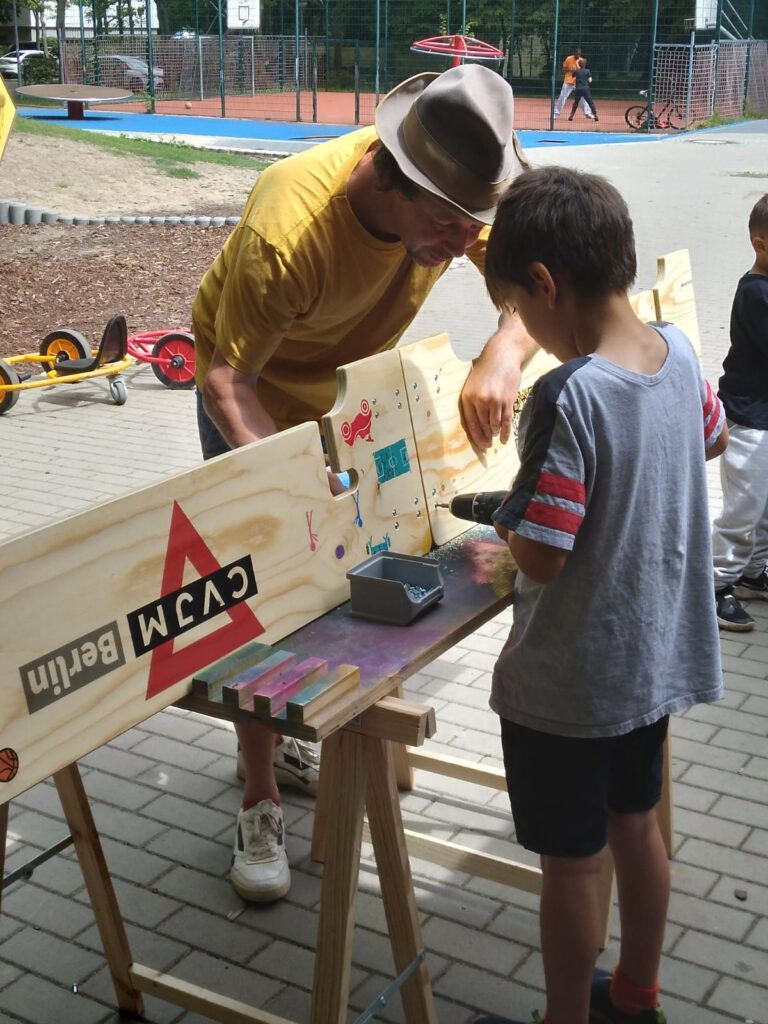 Anton zeigt einem Jungen wie man ein Scharnier anschraubt