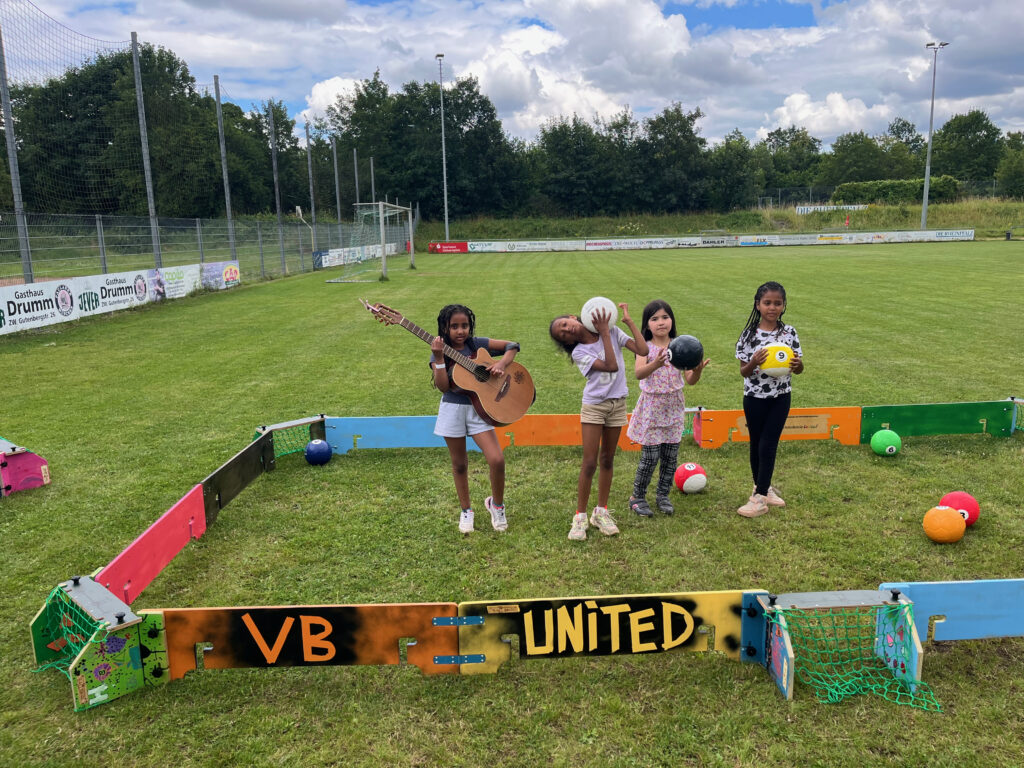 Kinder stehen in ihrer selbst gestalteten Ballbande und posen mit Gitarre für die Kamera